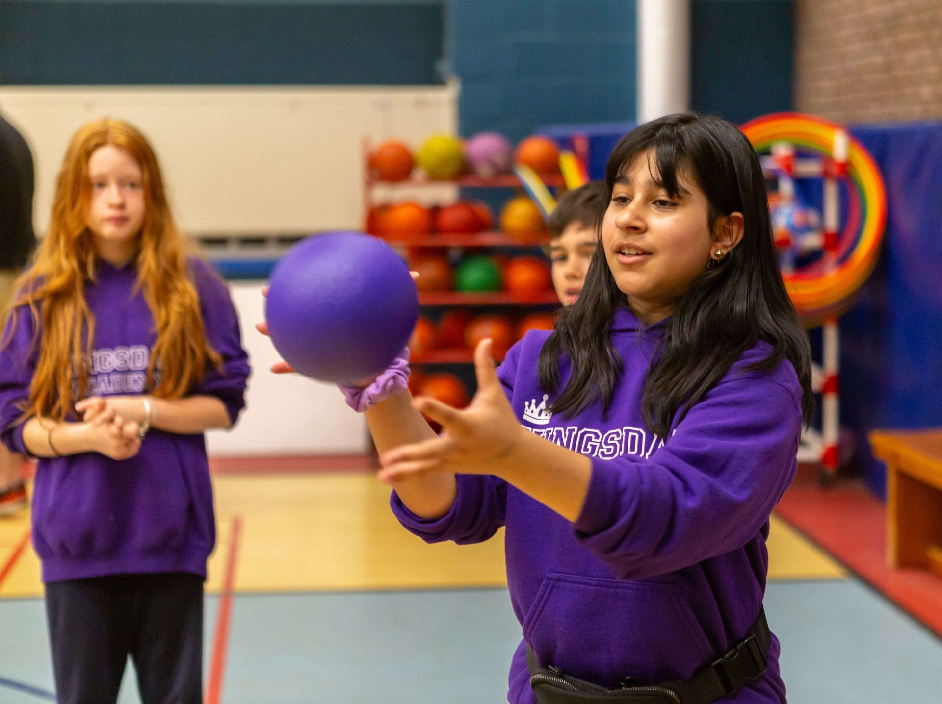 A girl in a purple sweatshirt is holding a purple ball in her hand.