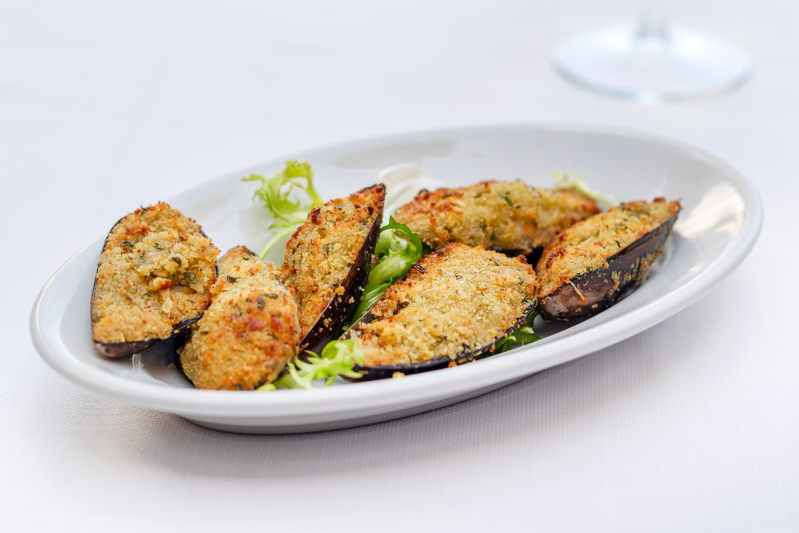 Cozze al forno con guscio su un piatto bianco, guarnite con lattuga.
