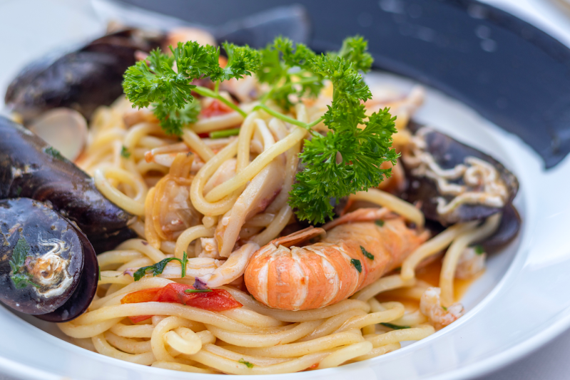 Pasta ai frutti di mare con cozze e gamberi, guarnita con prezzemolo, in una ciotola bianca.