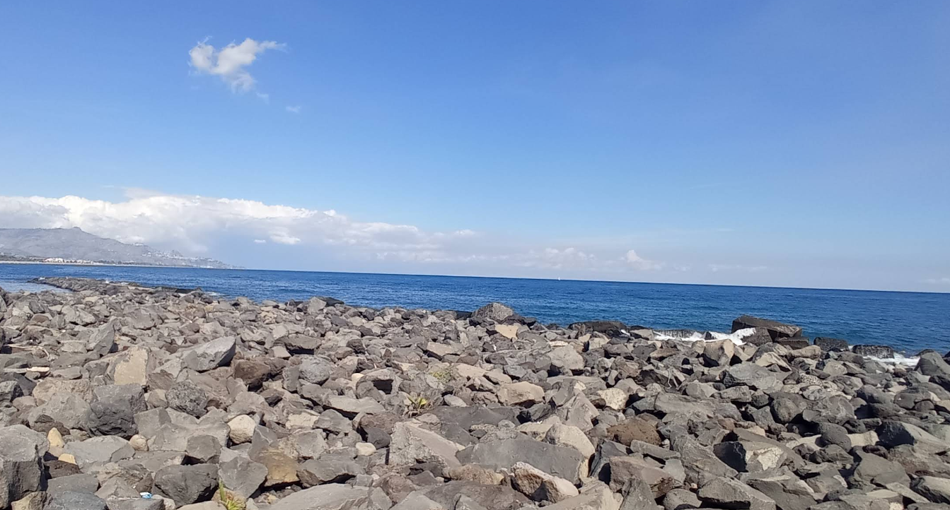 Costa rocciosa sotto un cielo azzurro brillante con qualche nuvola e l'oceano.