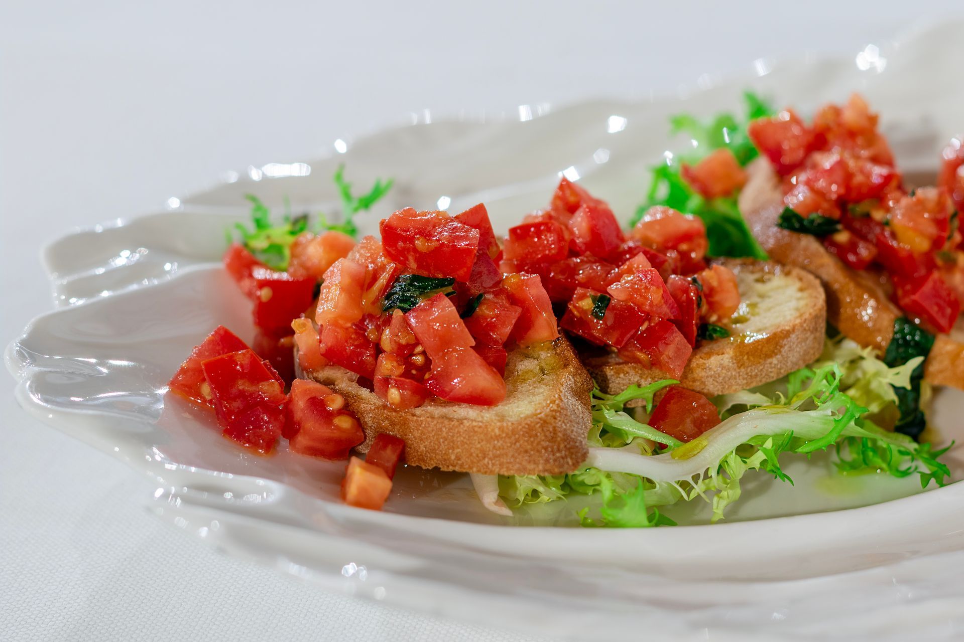 Antipasto di bruschetta: pane tostato condito con pomodori a cubetti, erbe aromatiche e olio d'oliva su un piatto bianco.