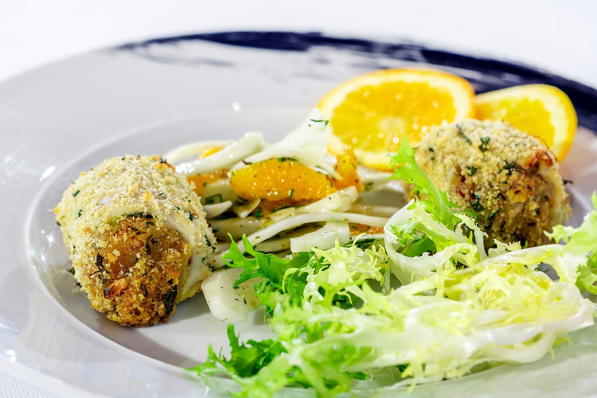 Tortini di granchio impanati con insalata di finocchio e arancia su un piatto bianco.