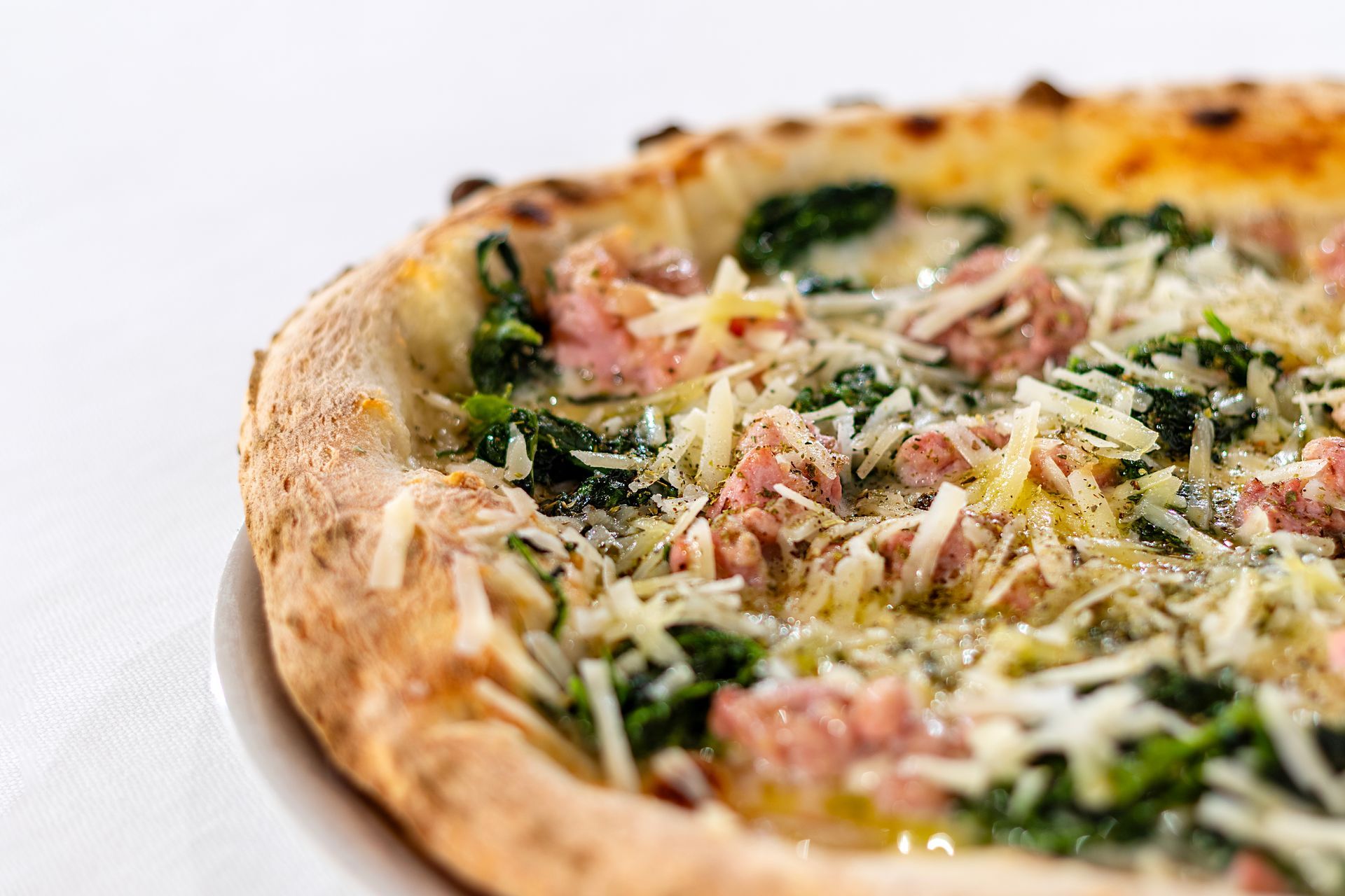 Pizza con salsiccia, spinaci e formaggio grattugiato su un piatto bianco.
