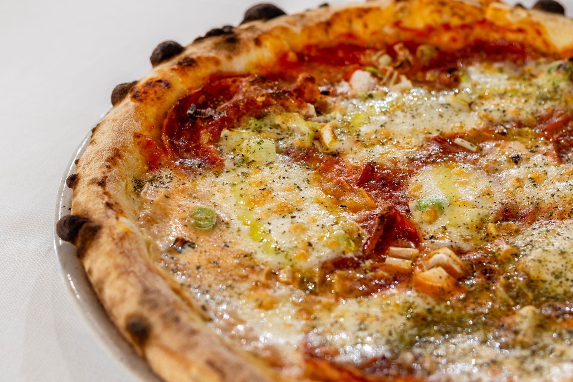 Primo piano di una pizza con crosta bruciacchiata, salsa di pomodoro, formaggio ed erbe aromatiche.