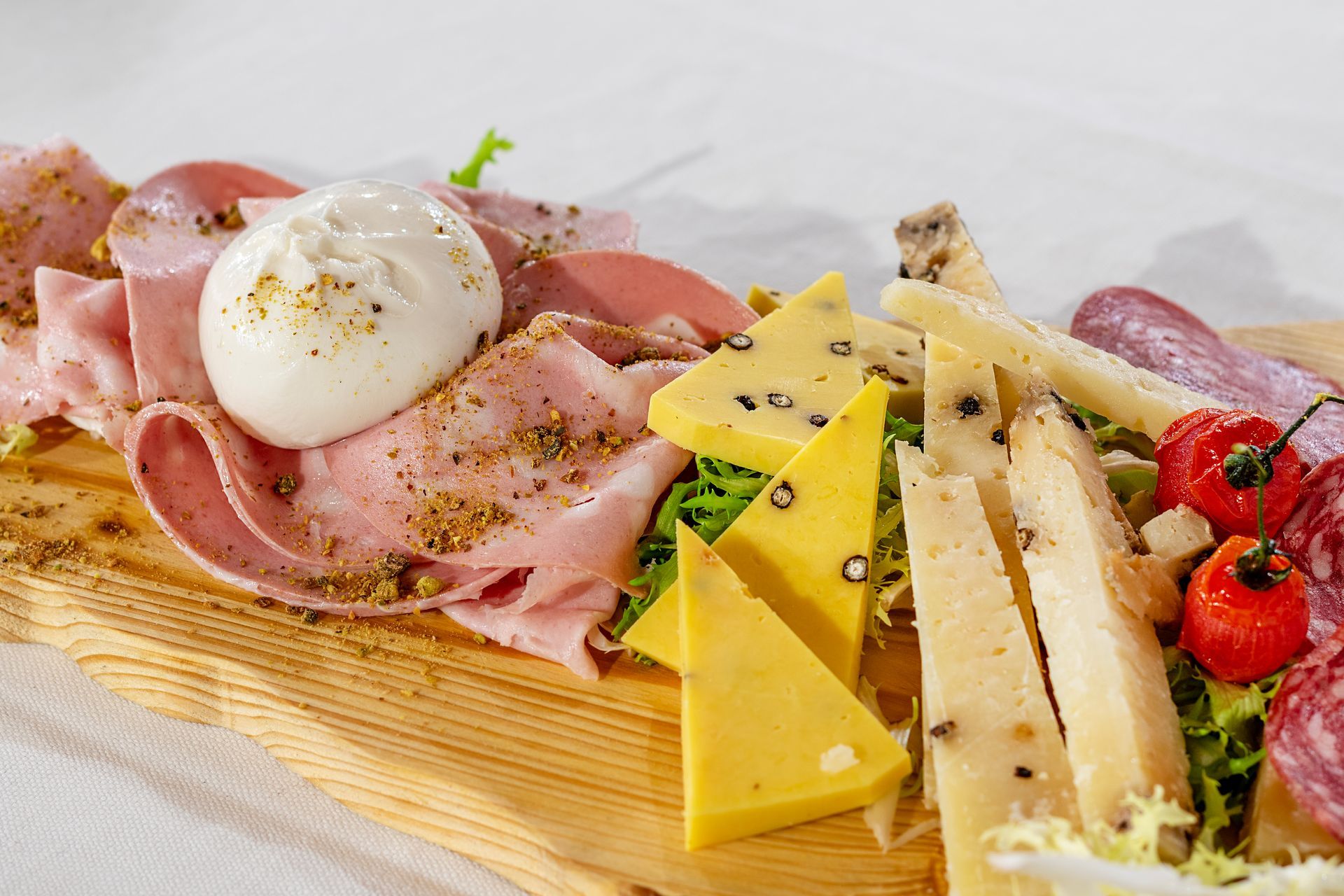 Tagliere di legno con salumi e formaggi italiani assortiti, tra cui prosciutto, salame e burrata.