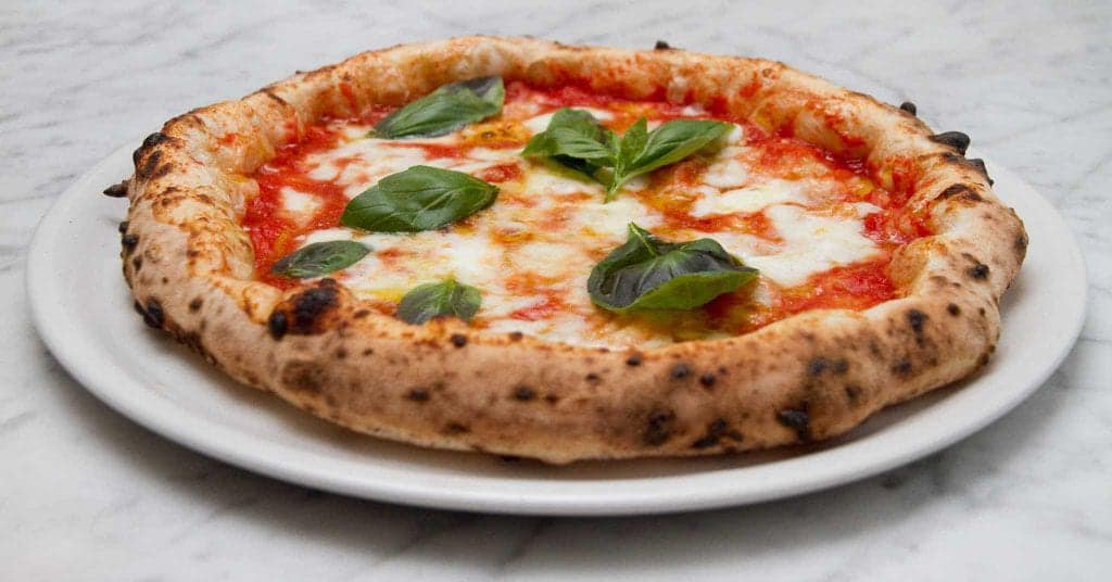 Pizza Margherita su un piatto bianco, guarnita con basilico, su un tavolo di marmo.