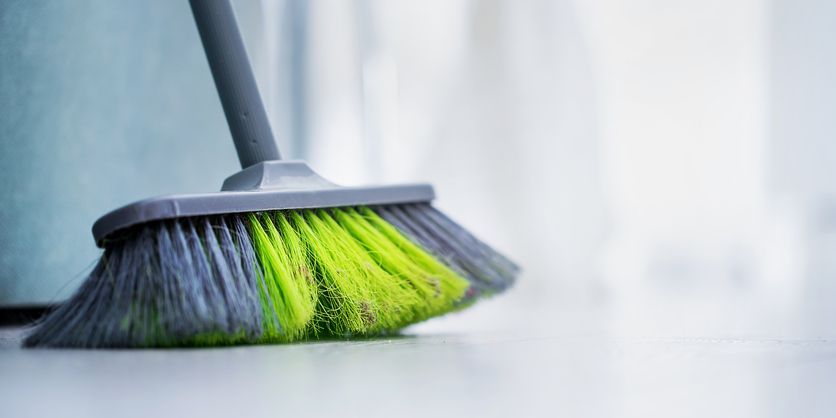Big broom with green hair stands on wooden office or home floor for cleaning room
