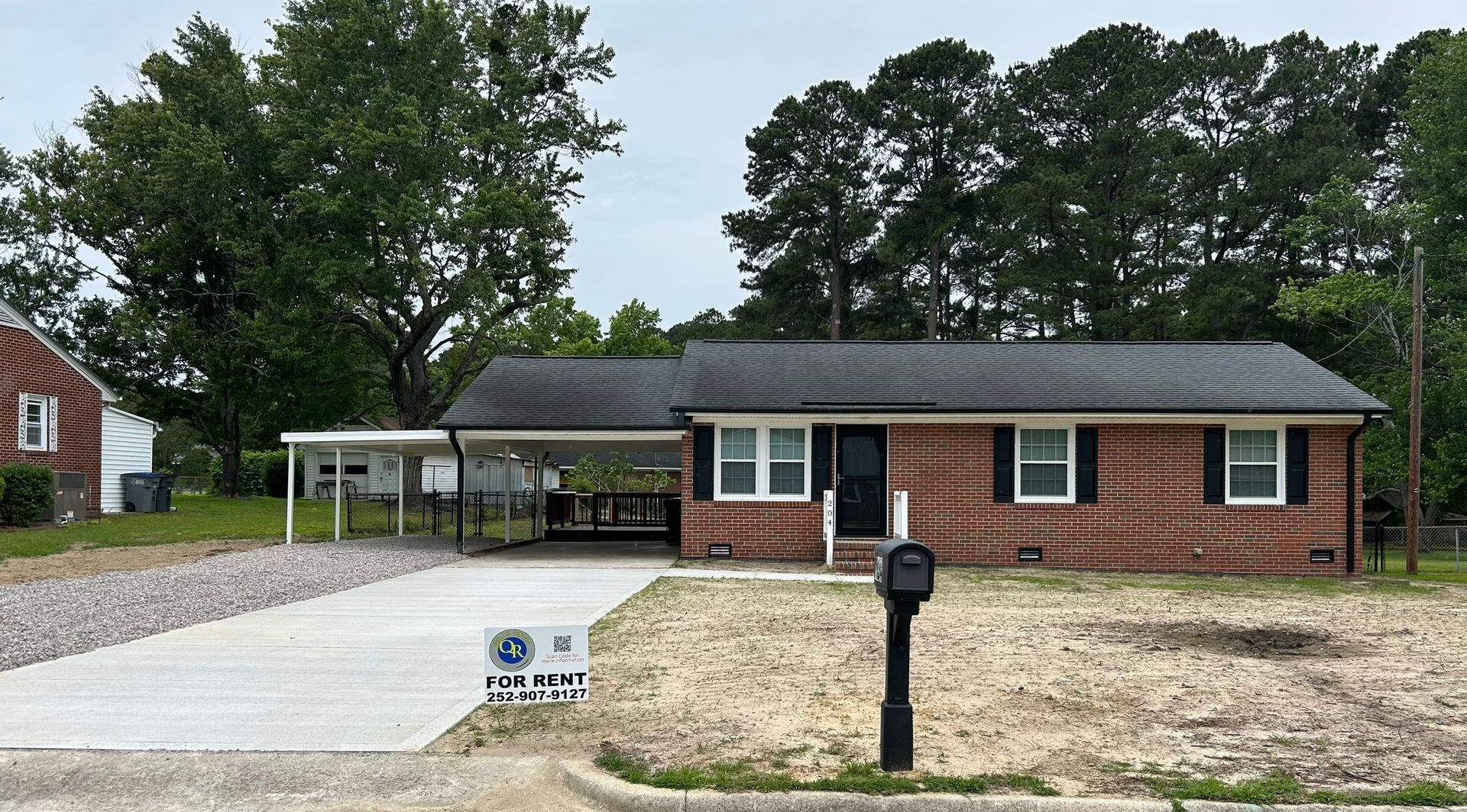 Brick ranch-style house with carport, mailbox, and gravel driveway on a cloudy day.