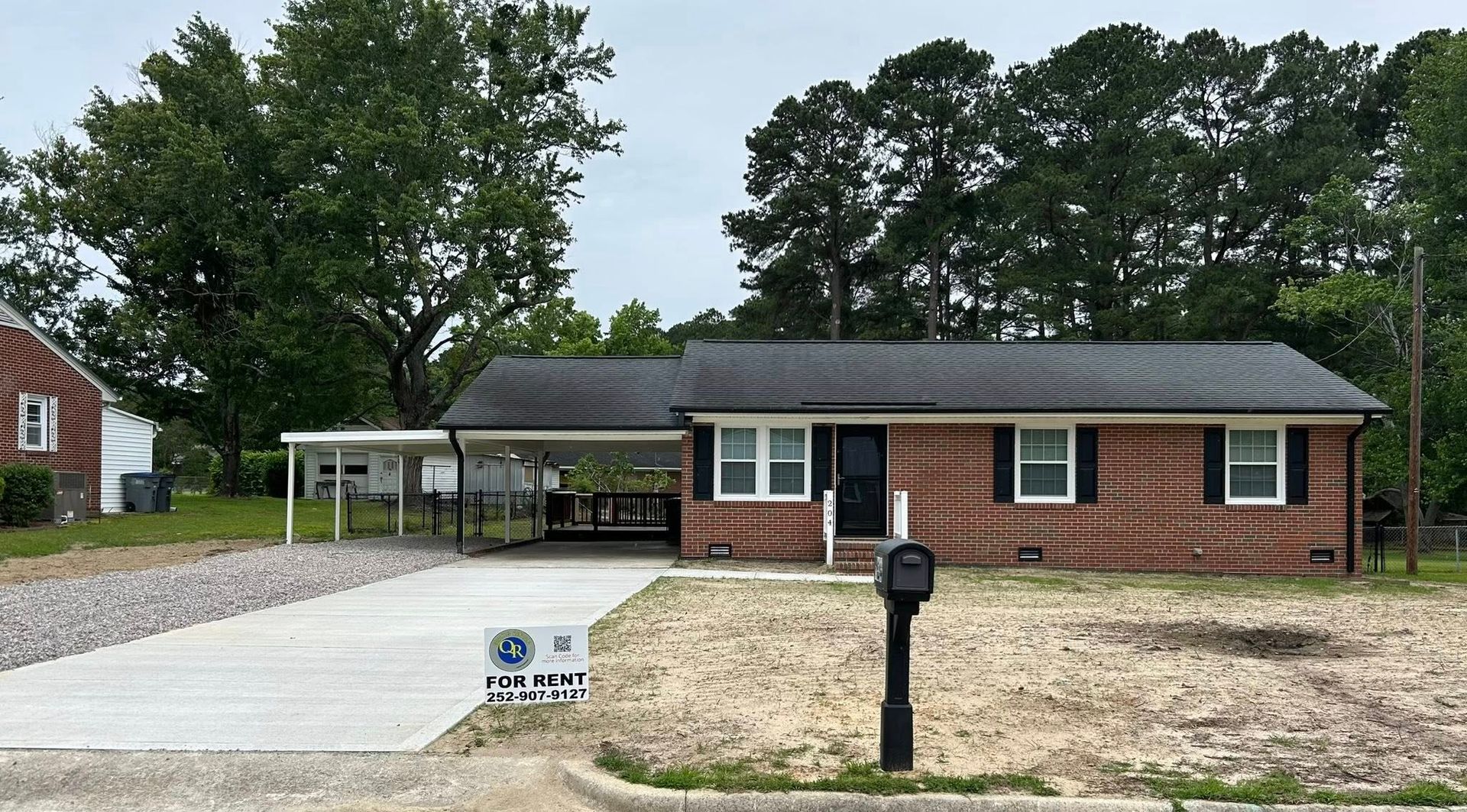 Brick house with a carport, gravel driveway, and mailbox in front.