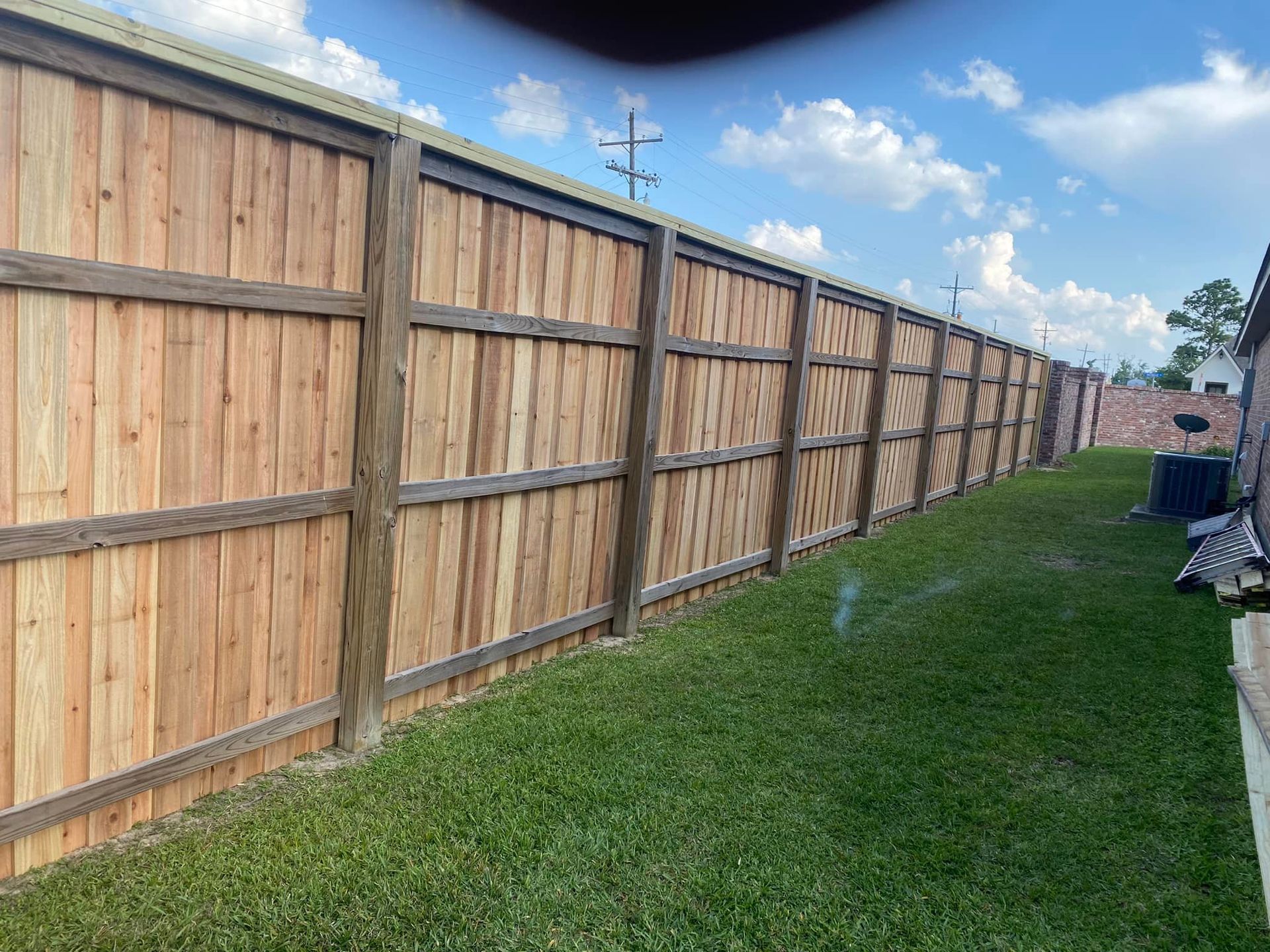 Wooden fence in a grassy yard, under a blue sky with clouds.