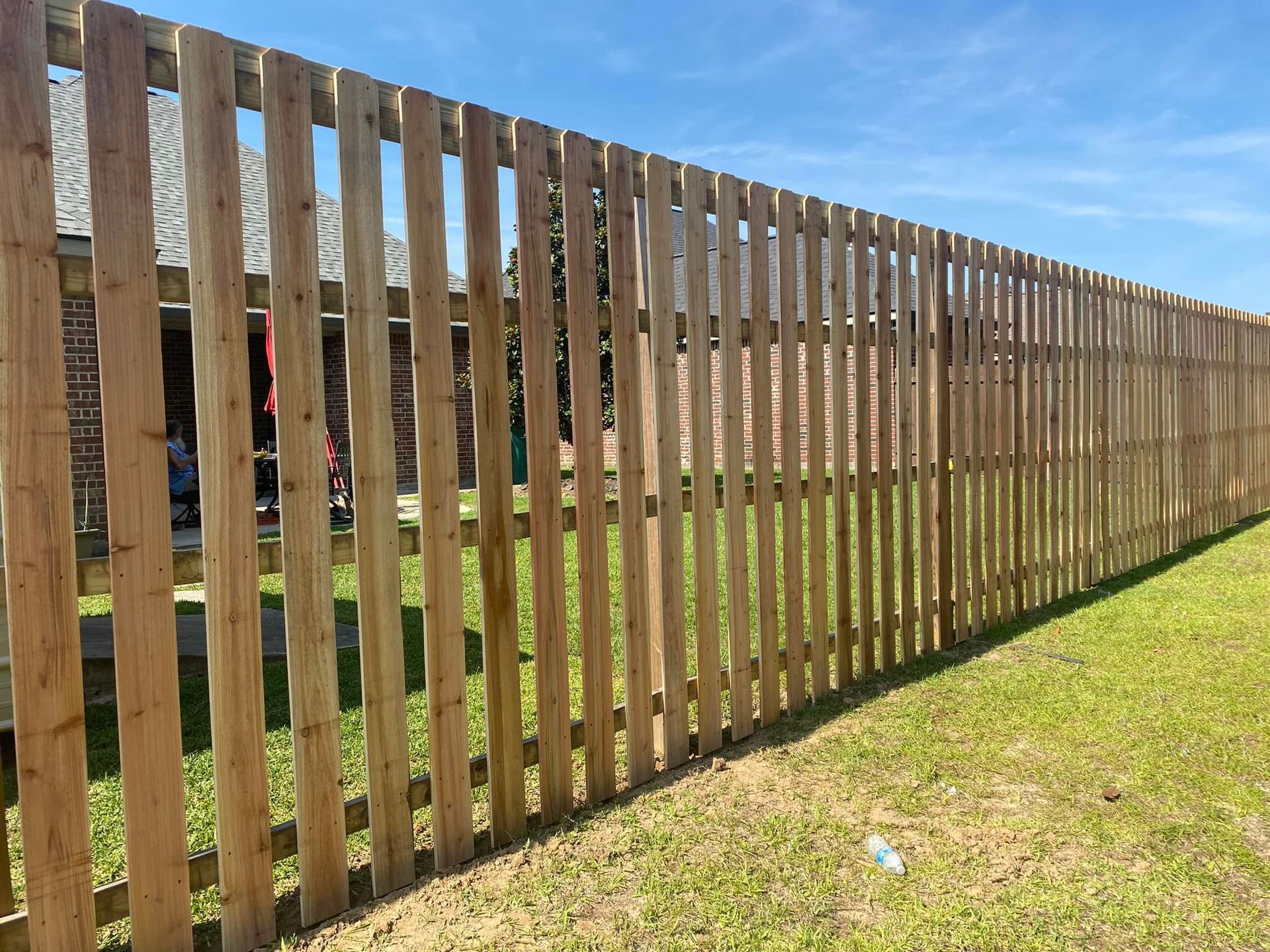 Wooden fence in a yard with green grass under a blue sky.