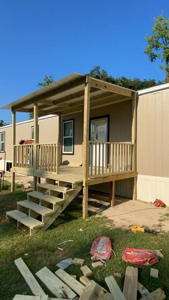 Wooden porch with steps and awning attached to a light brown mobile home, built outdoors on a sunny day.