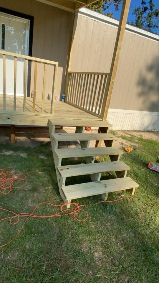 Wooden steps and deck attached to a light-colored building, built on grass.