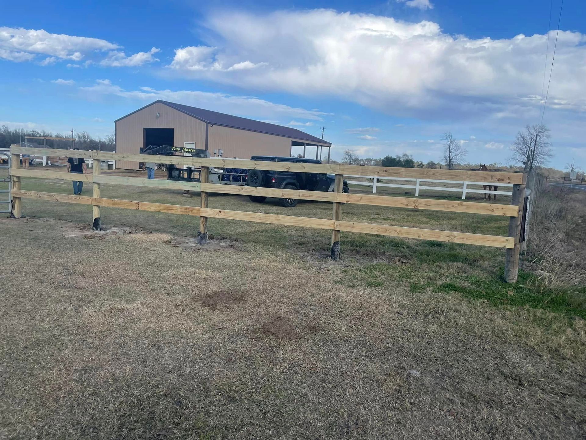 Wooden fence in field with barn and blue sky.