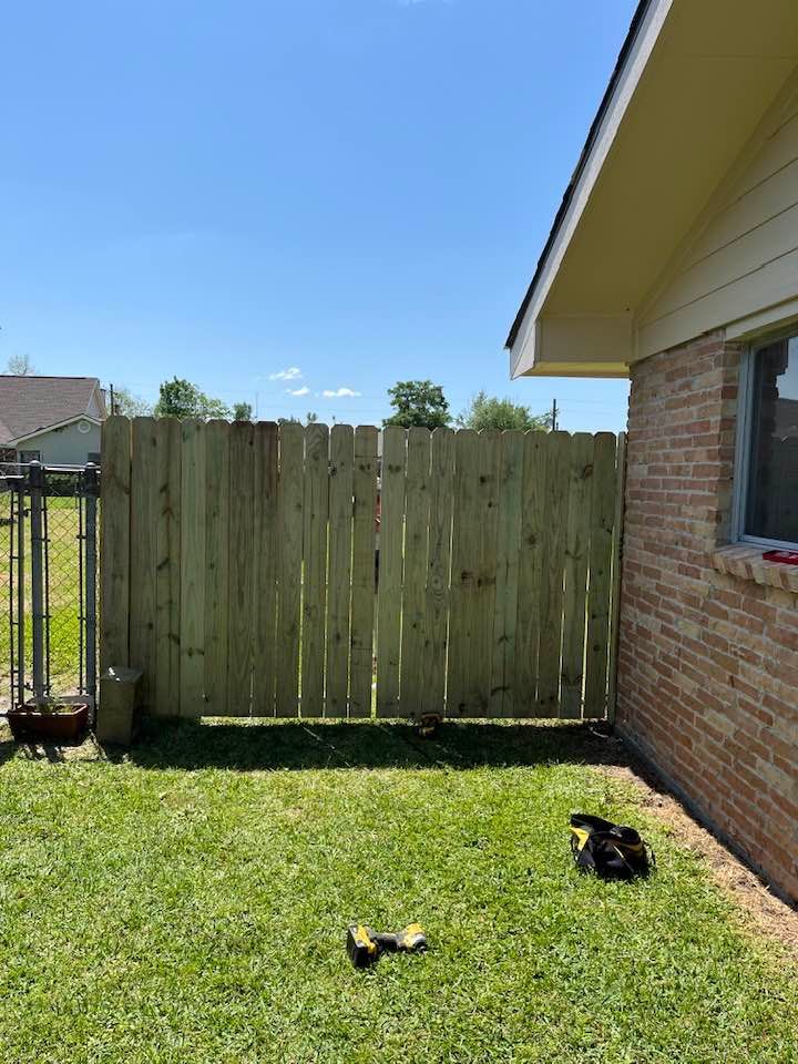 Wooden fence on green grass next to a brick house under a blue sky.