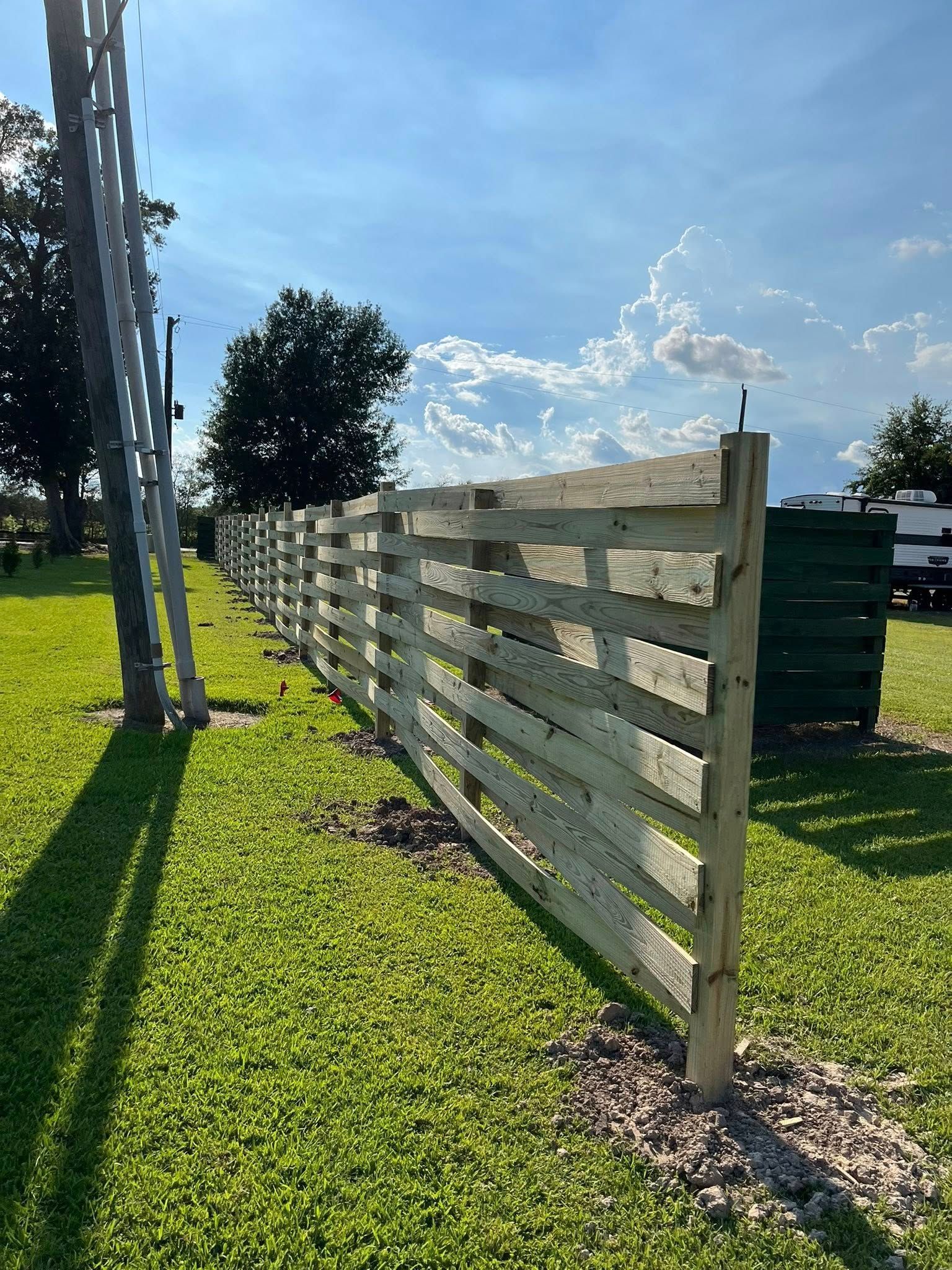 Wooden fence stretches across a grassy area under a partly cloudy sky.