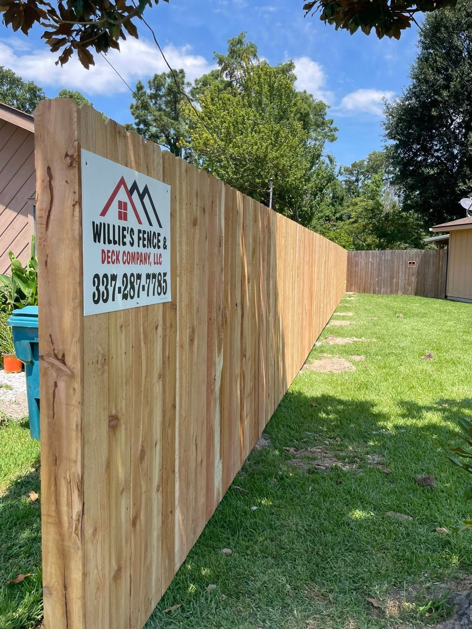 Wooden fence with company sign, green grass, and trees under a blue sky.