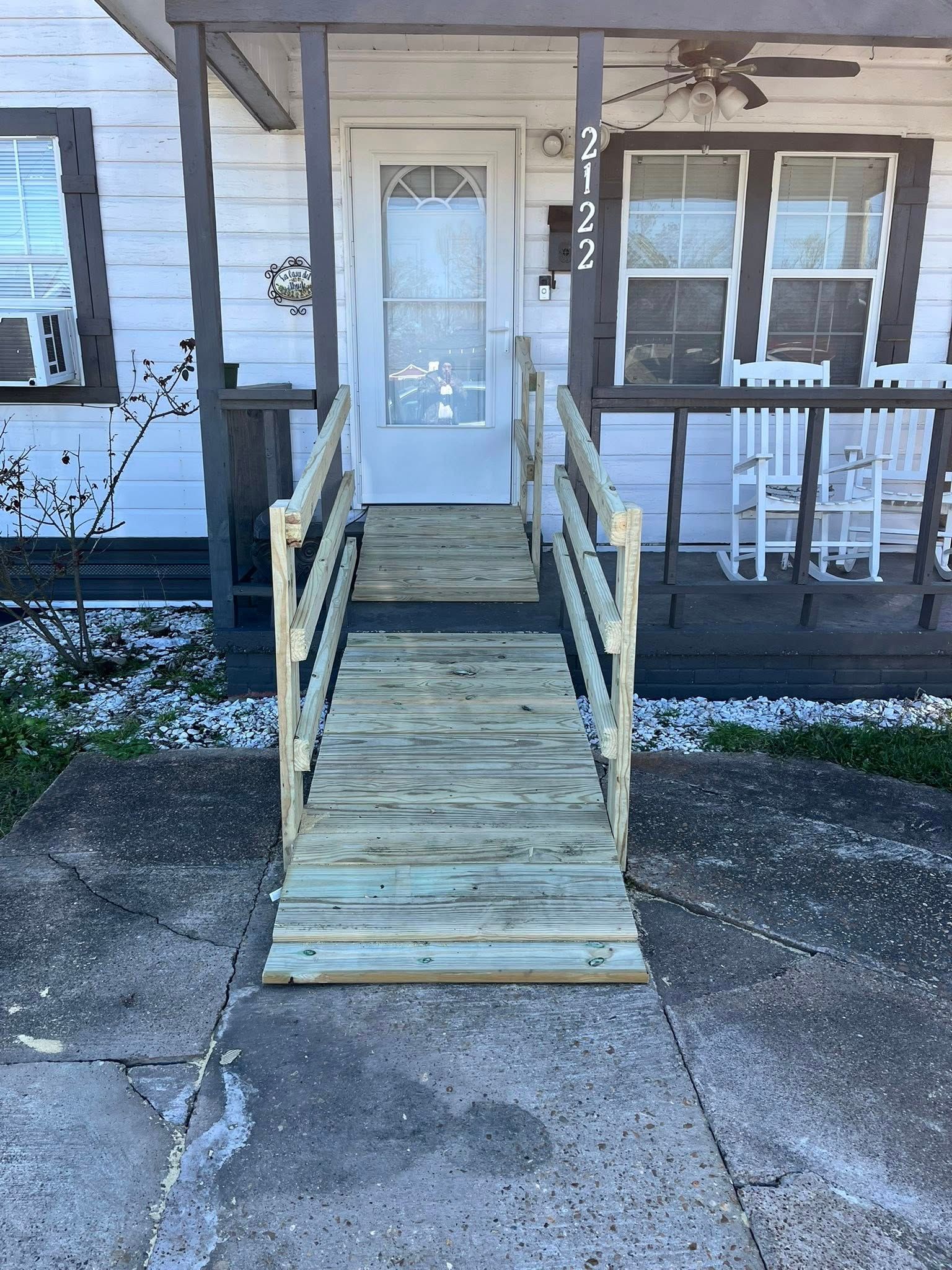 A wooden ramp with handrails leads up to the front door of a white house.