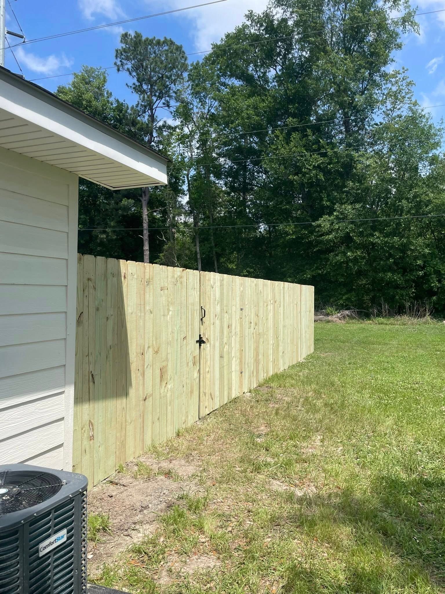 A wooden privacy fence borders a grassy backyard next to a light-colored house.