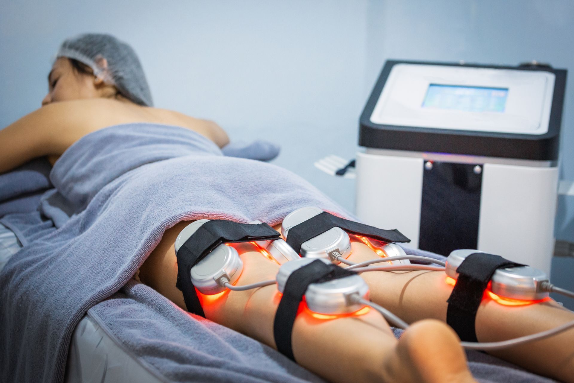 Una donna è sdraiata su un letto e si sta sottoponendo a un trattamento laser alle gambe.