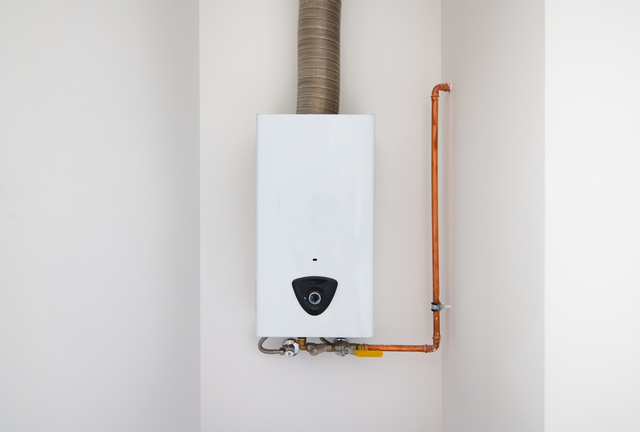 White wall-mounted gas water heater with copper pipes and ventilation duct.