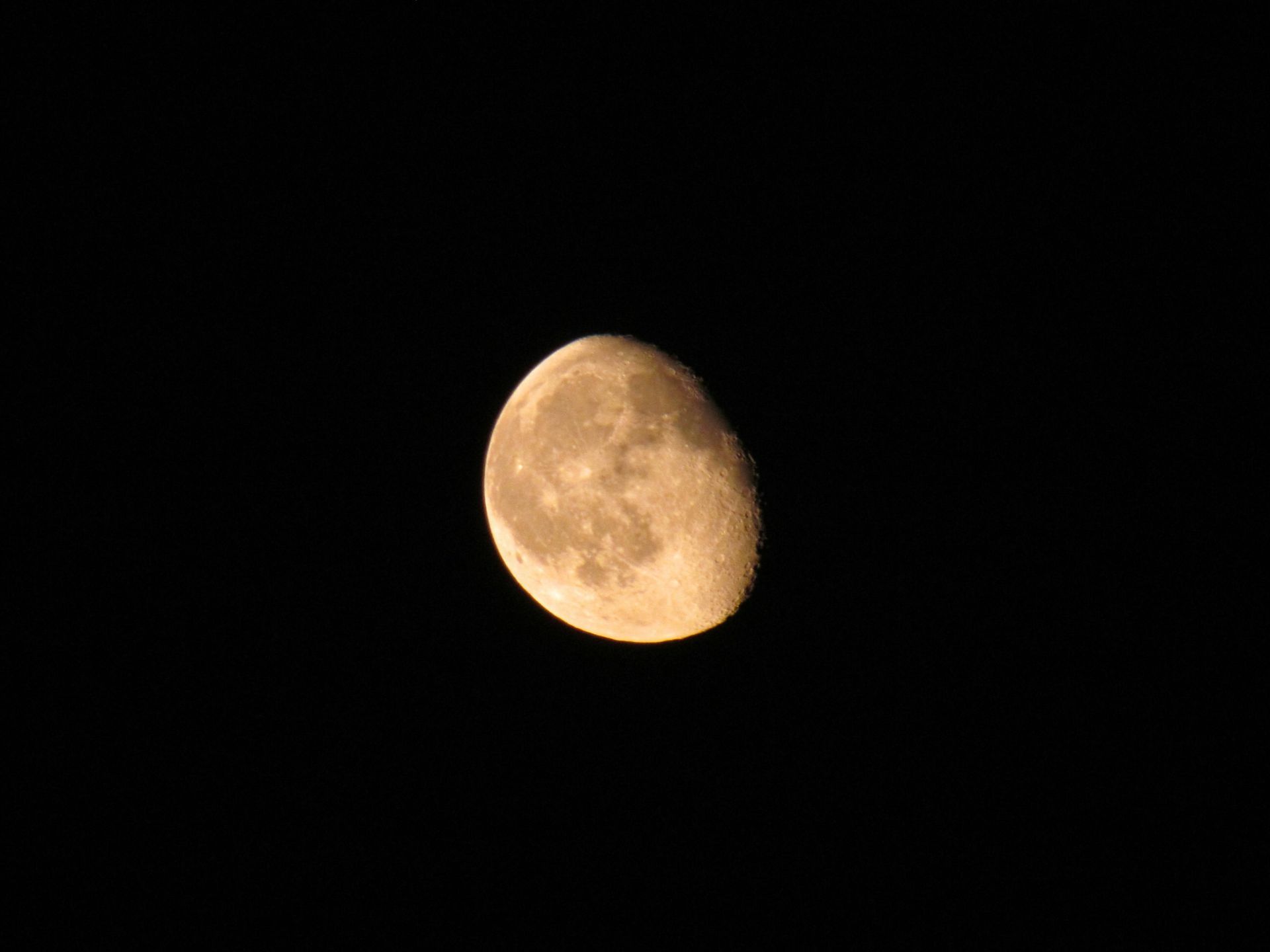 Nearly full moon with an amber light reflecting the moons surface over a dark background. 