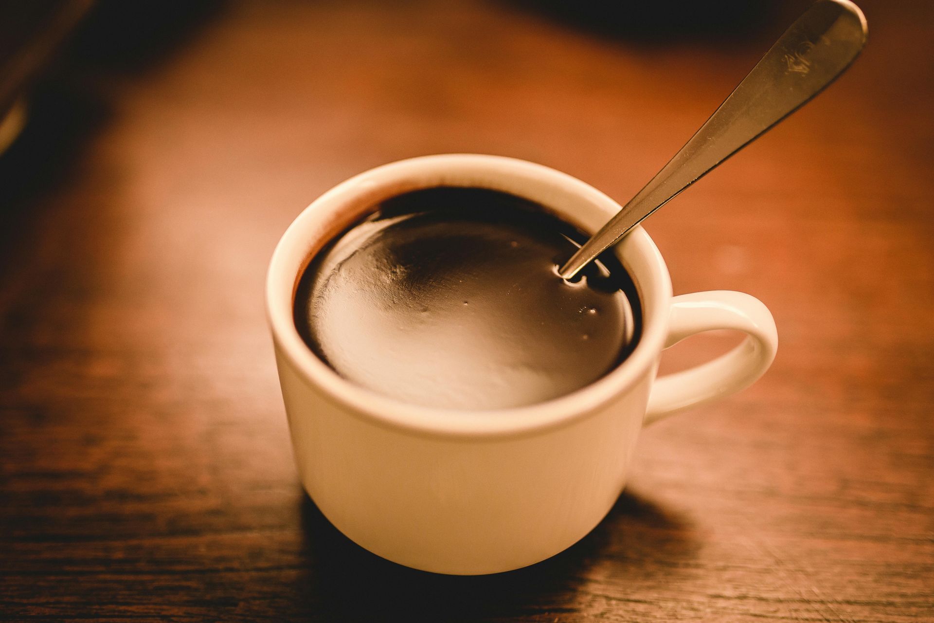 White mug with hot chocolate and a spoon, over a table