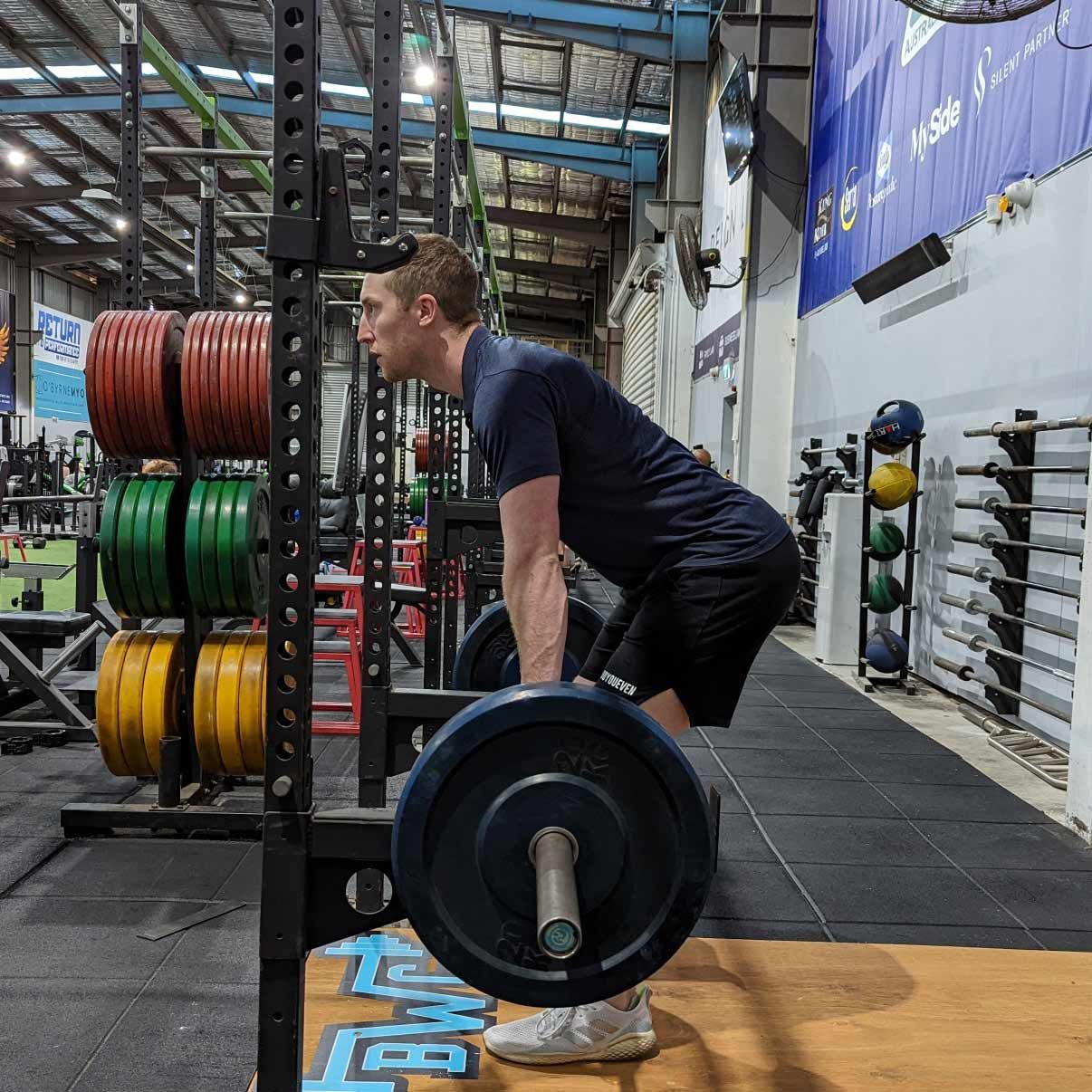 In a Gym, a Man Engages in Weightlifting, Lifting a Barbell From a Side View — Return to Performance Physiotherapy in Epsom, VIC