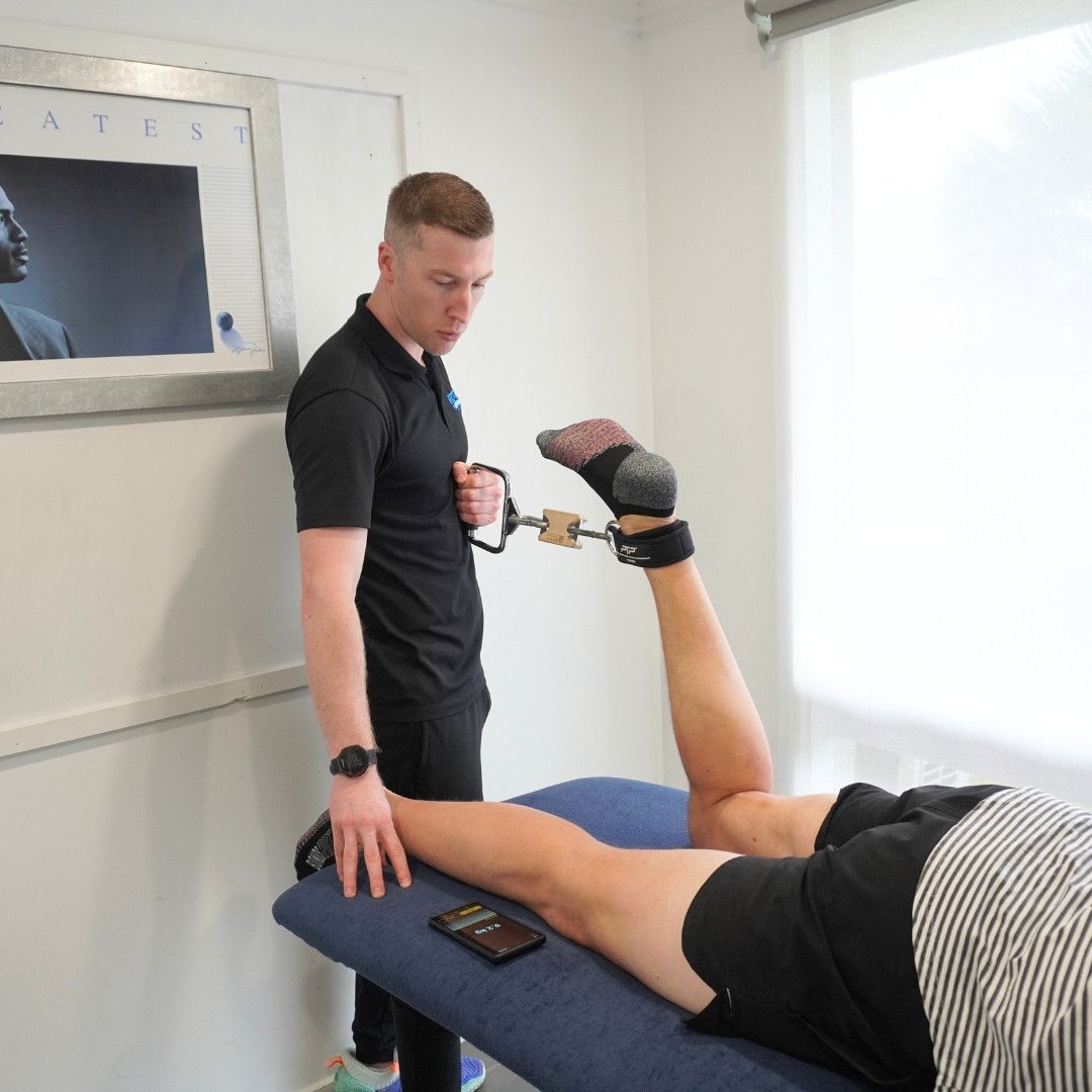 A Physical Therapist in a Black Shirt Uses a Hand-held Resistance Device — Return to Performance Physiotherapy in Epsom, VIC