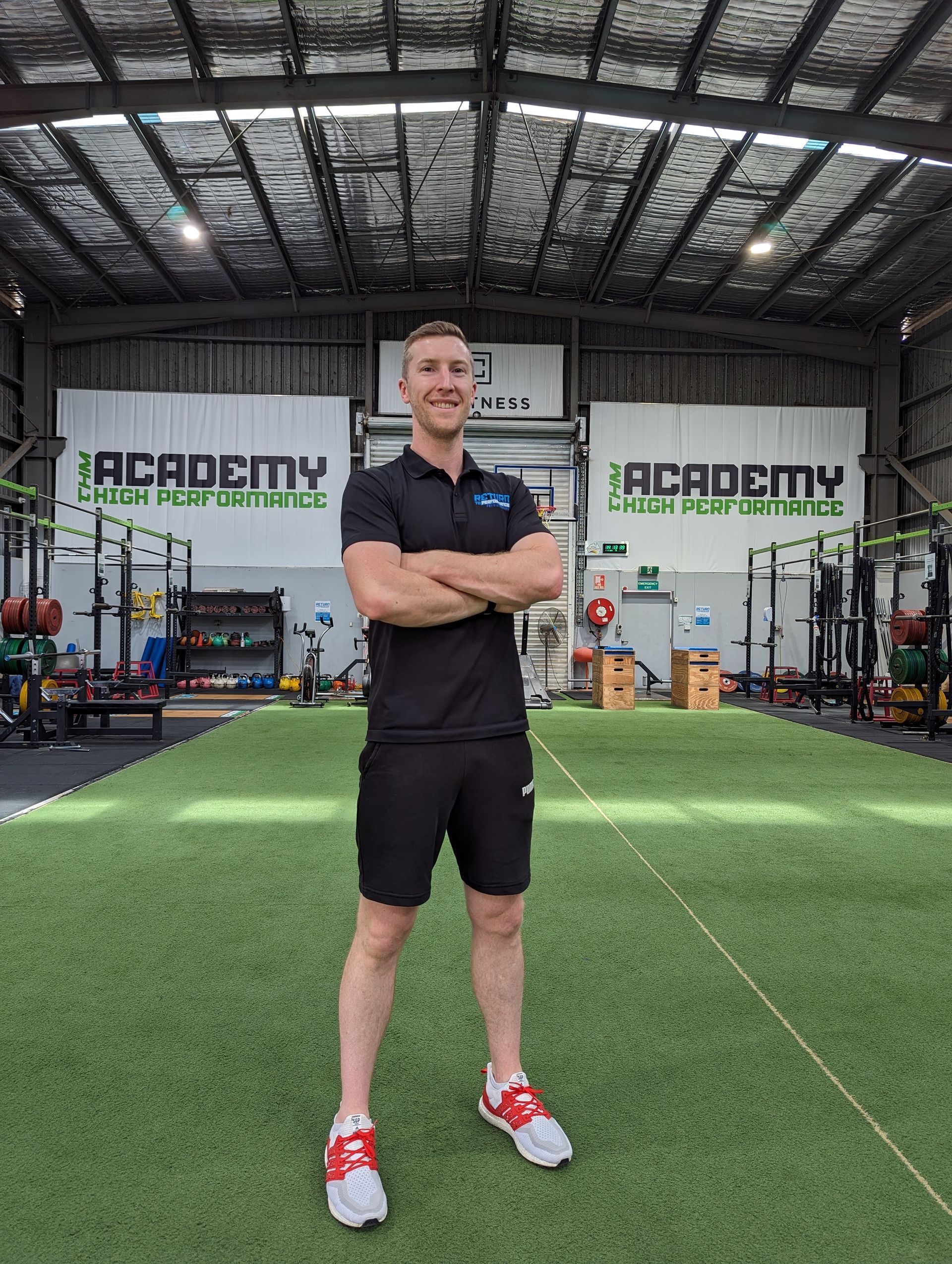 A Man Is Standing In A Gym With His Arms Crossed — Return to Performance Physiotherapy in Epsom, VIC