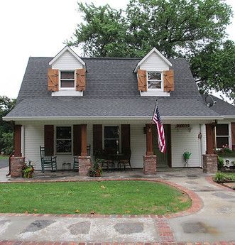 Small brick house with a gray roof, two dormers, front porch, and an American flag by the door.