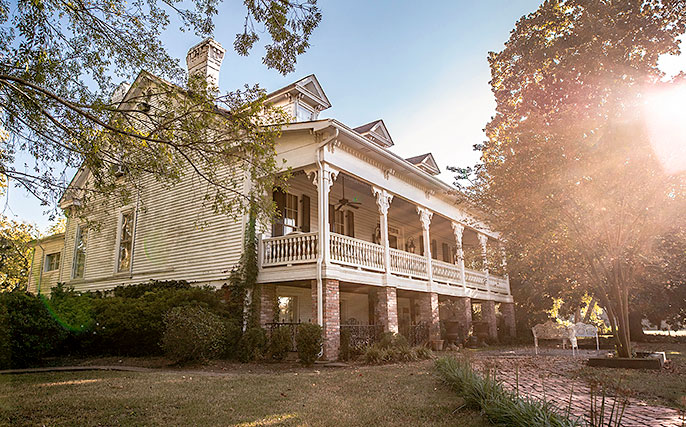 White Victorian house with a wraparound porch in a sunny, tree-lined yard