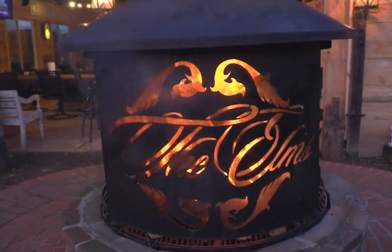 Decorative black metal fire pit glowing with orange flames and script cutout at dusk