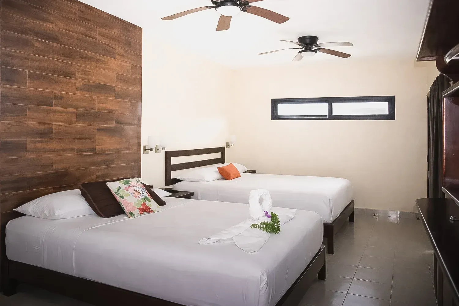 Habitación de hotel moderna con dos camas individuales, pared decorativa de madera, ventiladores de techo.