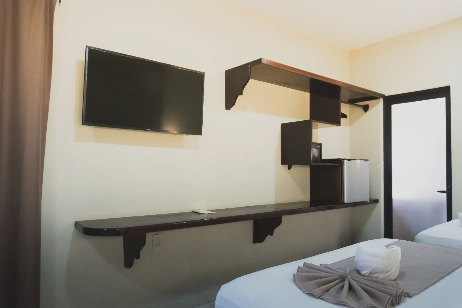 Habitación de hotel minimalista con televisor montado en la pared, escritorio, cama y puerta abierta al baño.