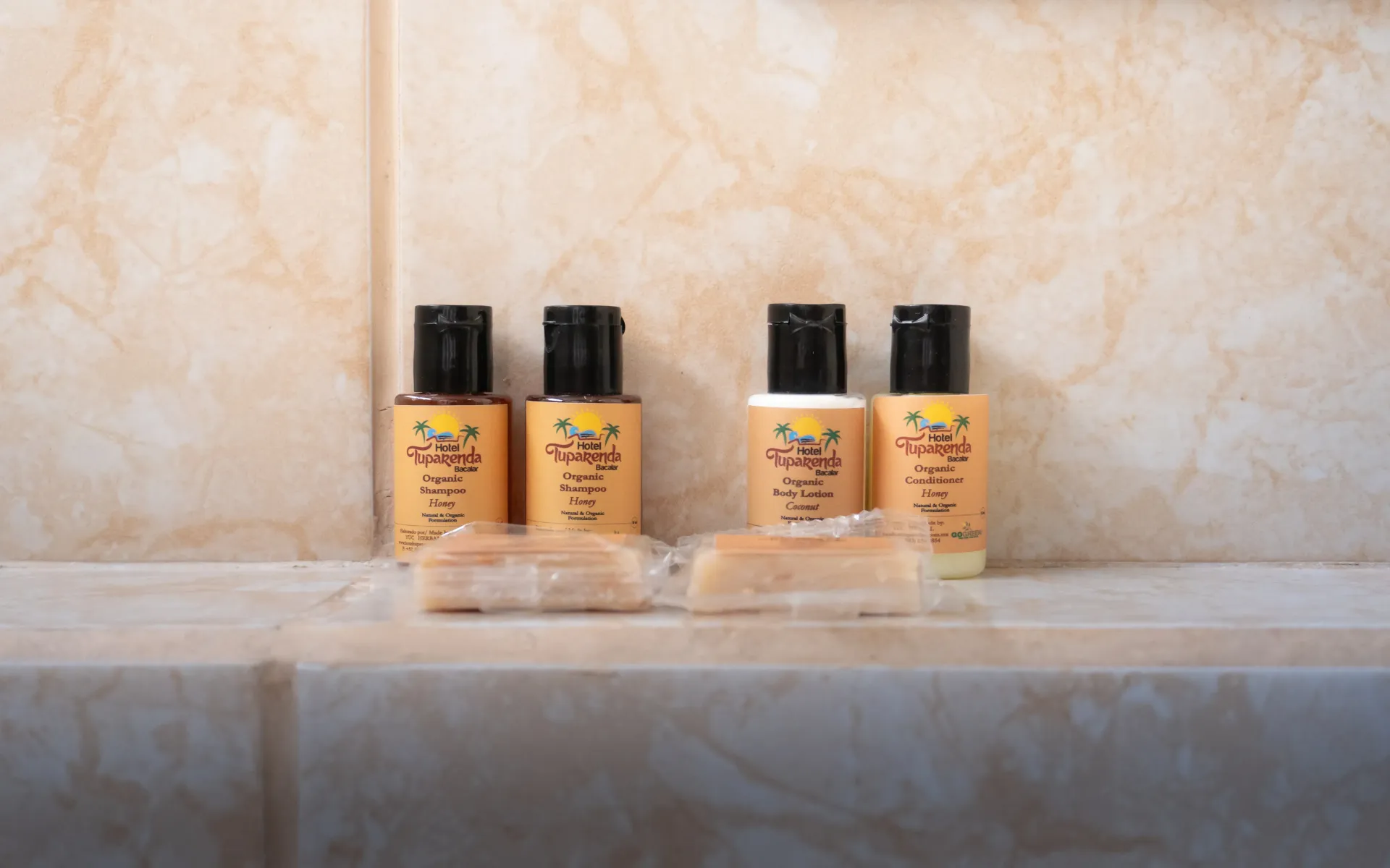 Cuatro pequeñas botellas de color ámbar con tapones negros sobre una repisa de mármol, junto a una pared de piedra beige.