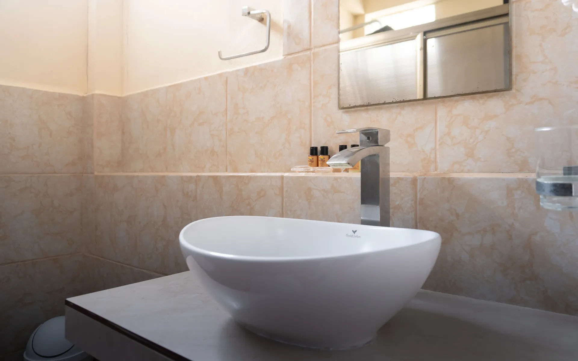 Lavabo moderno con lavabo blanco sobre encimera, grifo cromado, paredes alicatadas en color beige y espejo sobre la encimera.