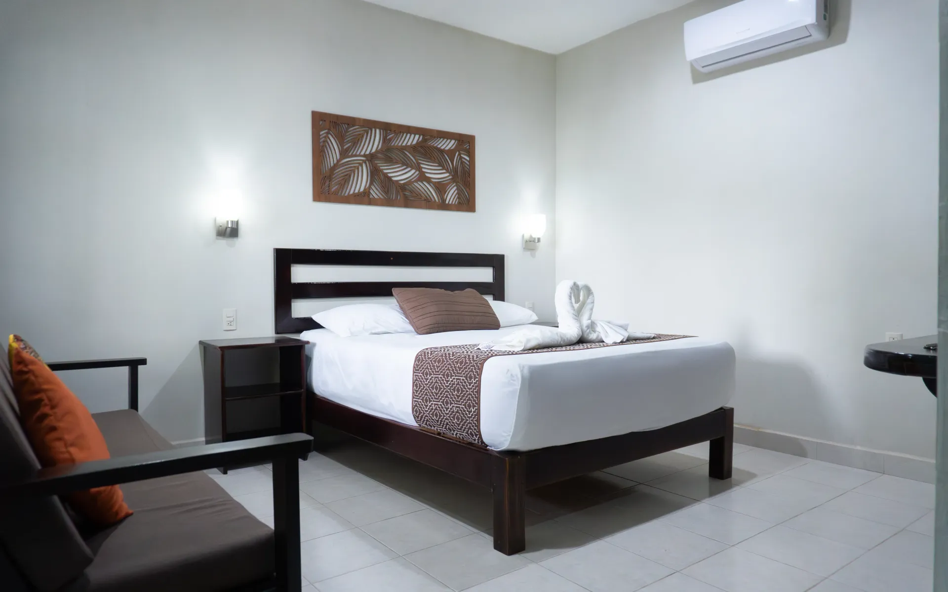 Habitación de hotel minimalista con una cama bien hecha, muebles negros y paredes blancas.