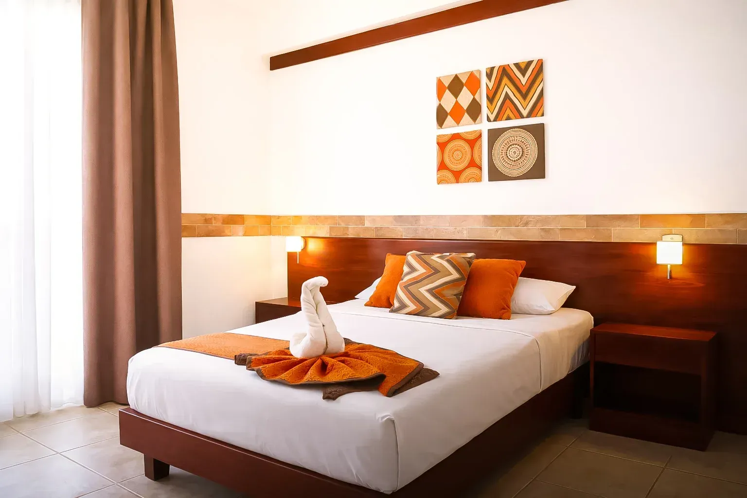 Modern hotel bedroom with a neatly made bed, orange accents, wood headboard, and wall art