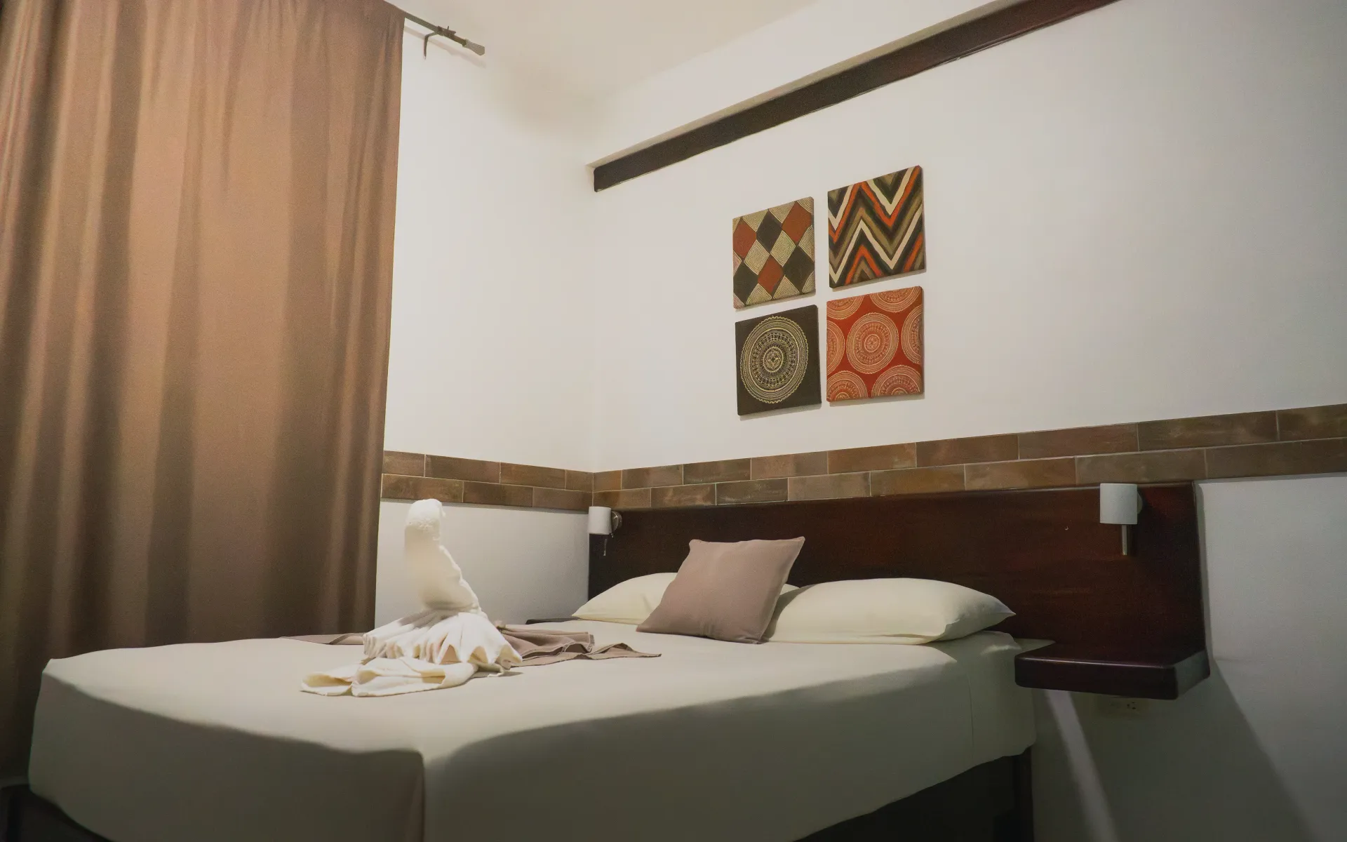 Cama de habitación de hotel bien hecha con almohadas, cuadros en la pared y cortinas marrones en una acogedora habitación.