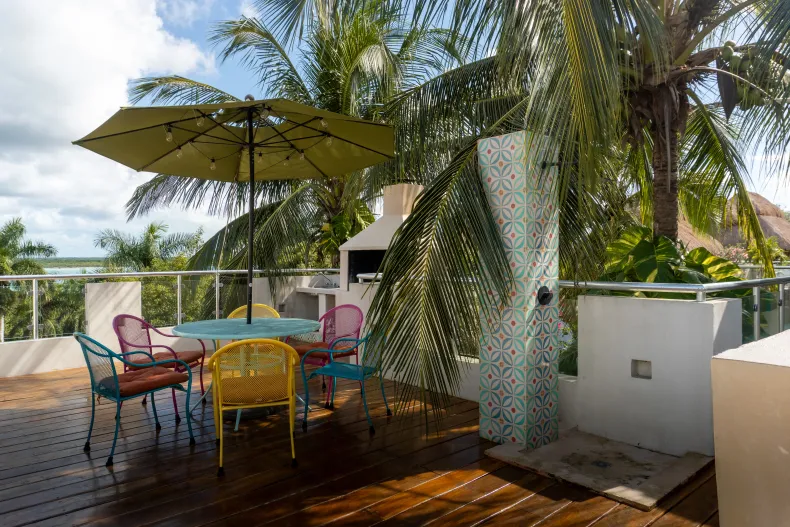 Muebles de patio coloridos bajo una gran sombrilla junto a una palmera y ducha exterior en una terraza soleada.