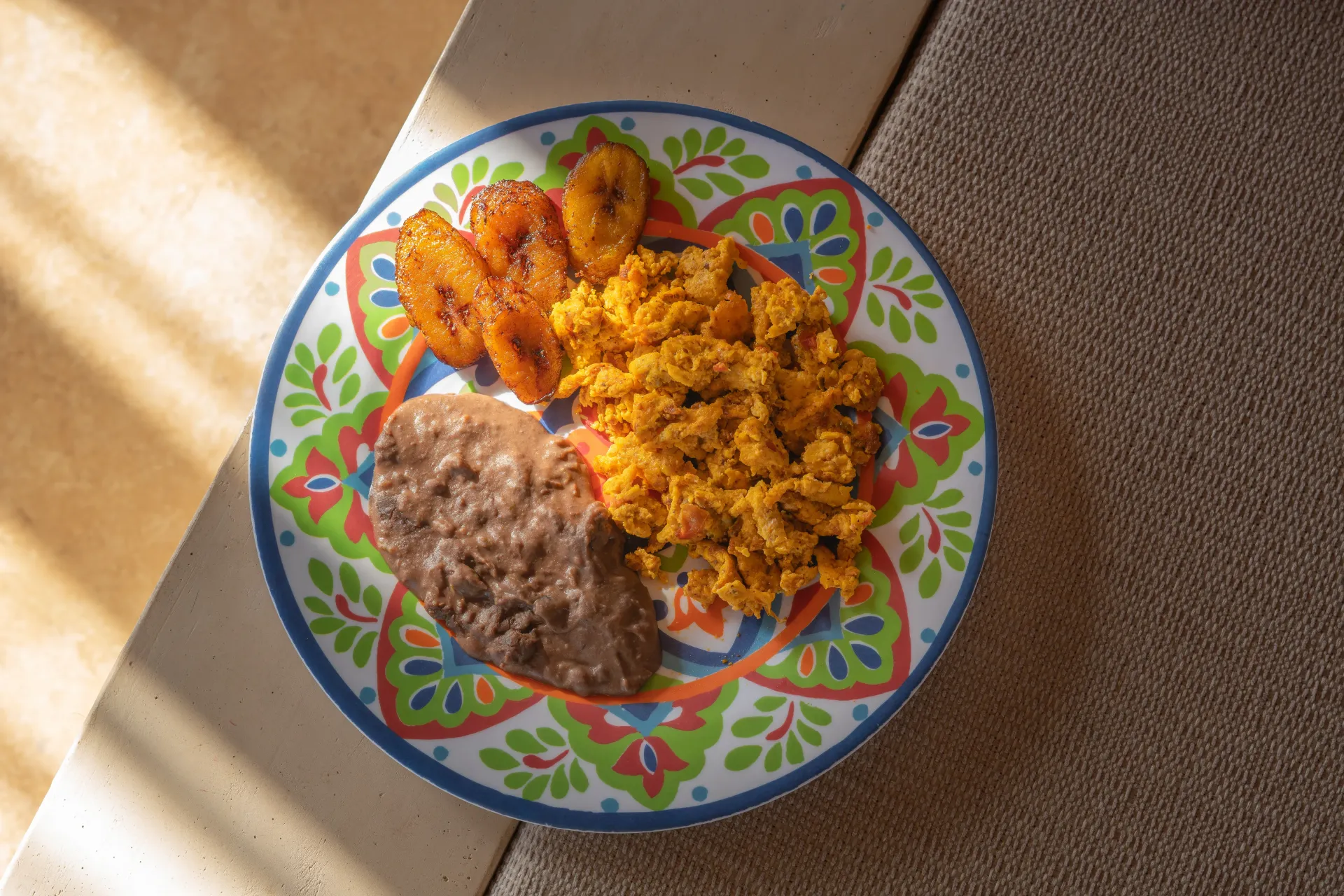 Plato con arroz, frijoles y plátanos bajo la cálida luz del sol sobre una mesa.