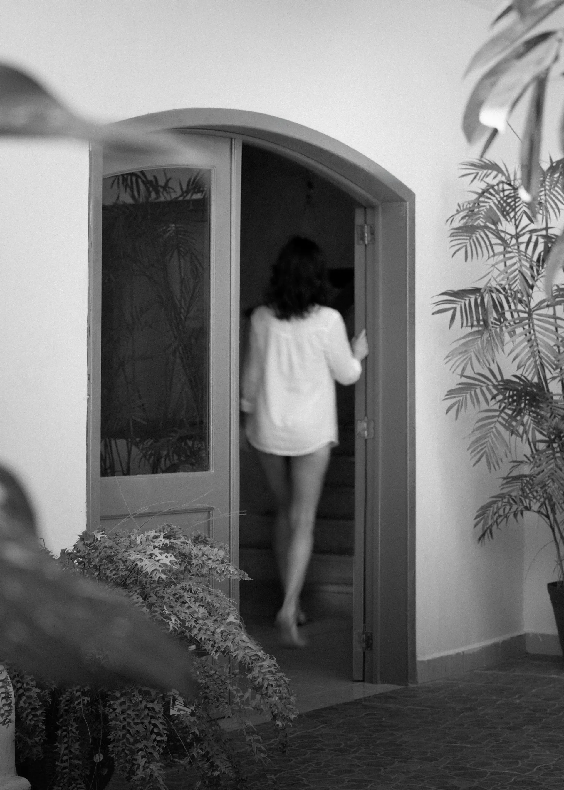 Una mujer atraviesa un arco que da a un patio interior con poca luz.