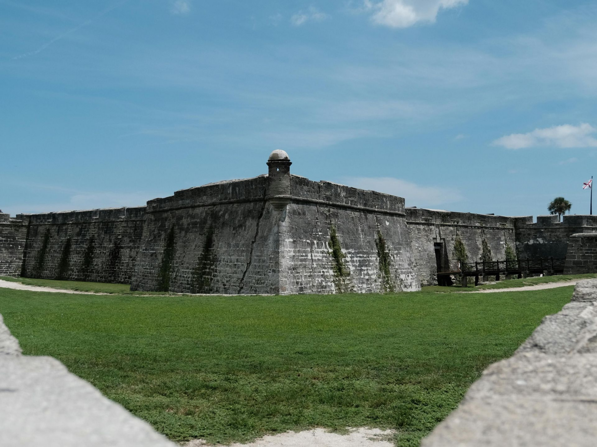 Fortaleza con murallas de piedra y bastión rodeados de hierba verde bajo un cielo azul.