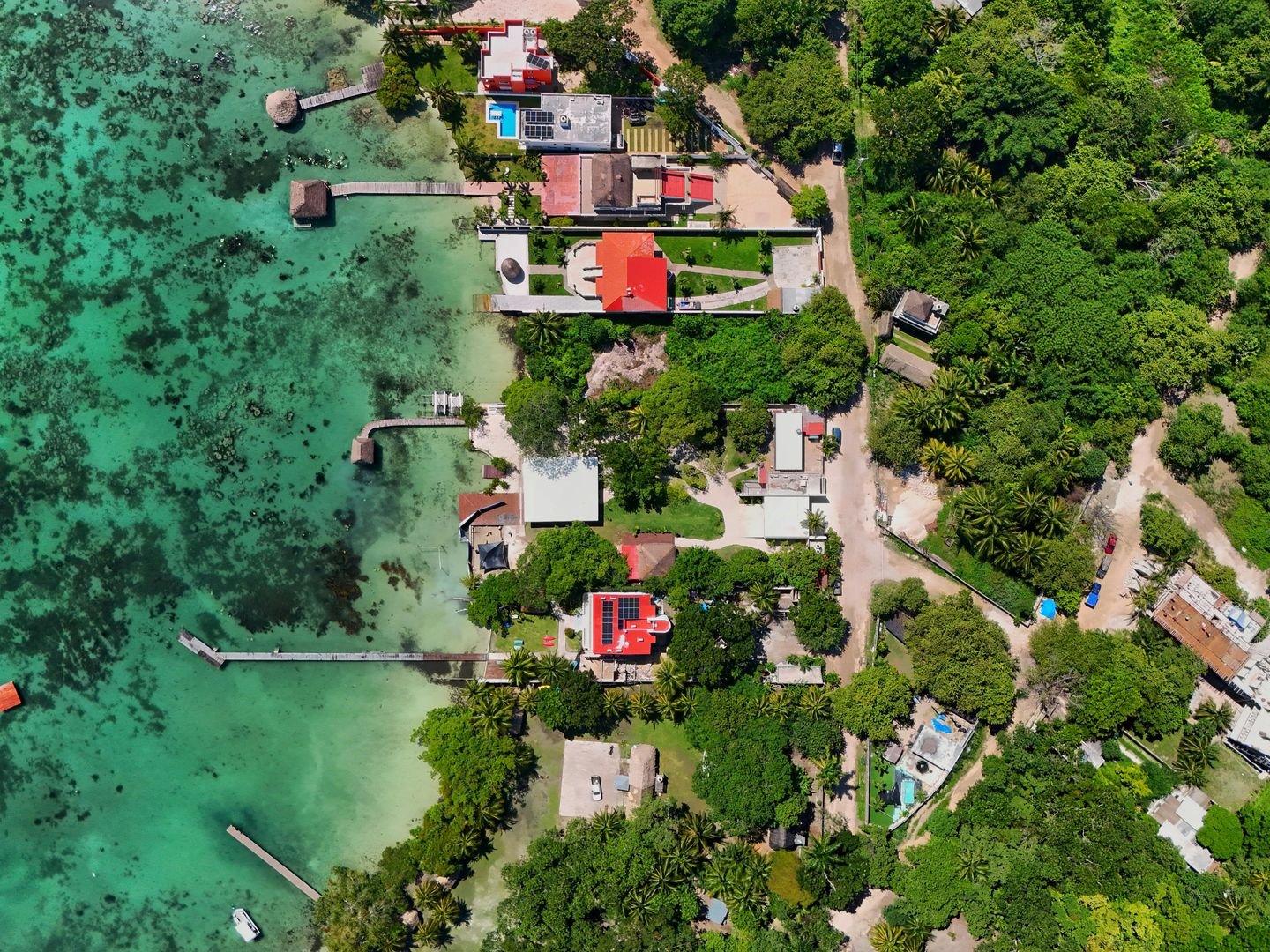 Vista aérea de una costa tropical con aguas turquesas, muelles y pequeñas casas entre densos árboles verdes.