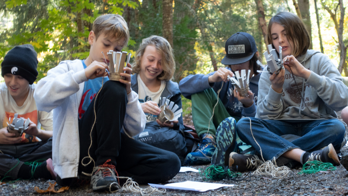 Young teens sitting on the forest floor learning basket weaving techniques from Lomakatsi educators.