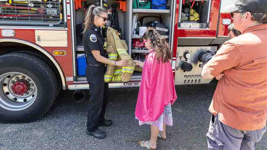 Female fire fighter, standing in front of a fire truck, showing her uniform to a young girl at Sparking Action event at ScienceWorks.