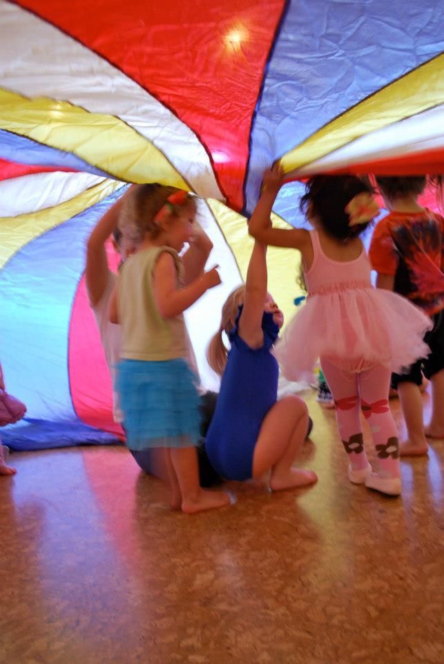 young children dancing under a rainbow parachute