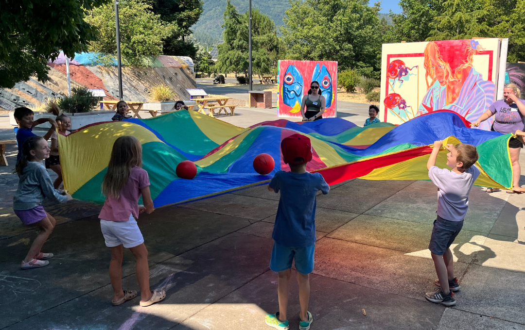 a group of ScienceWorks summer campers playing with a rainbow parachute