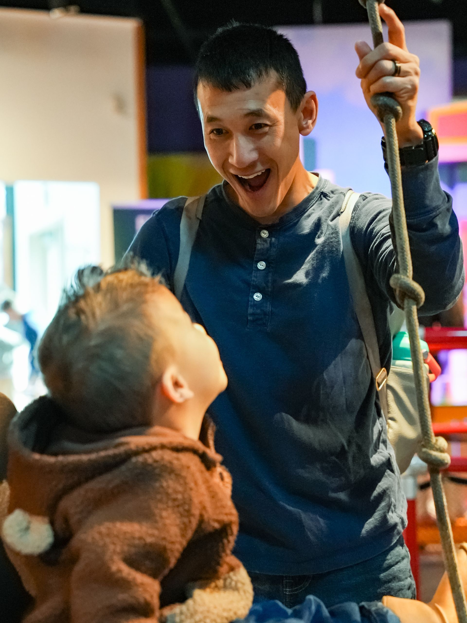 Man smiling at a child, holding a rope in an indoor setting at ScienceWorks.